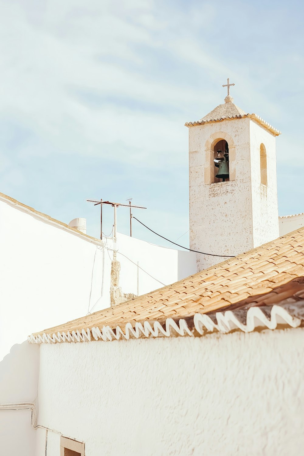 Whitewashed bell tower with a terracotta roof against a clear blue sky